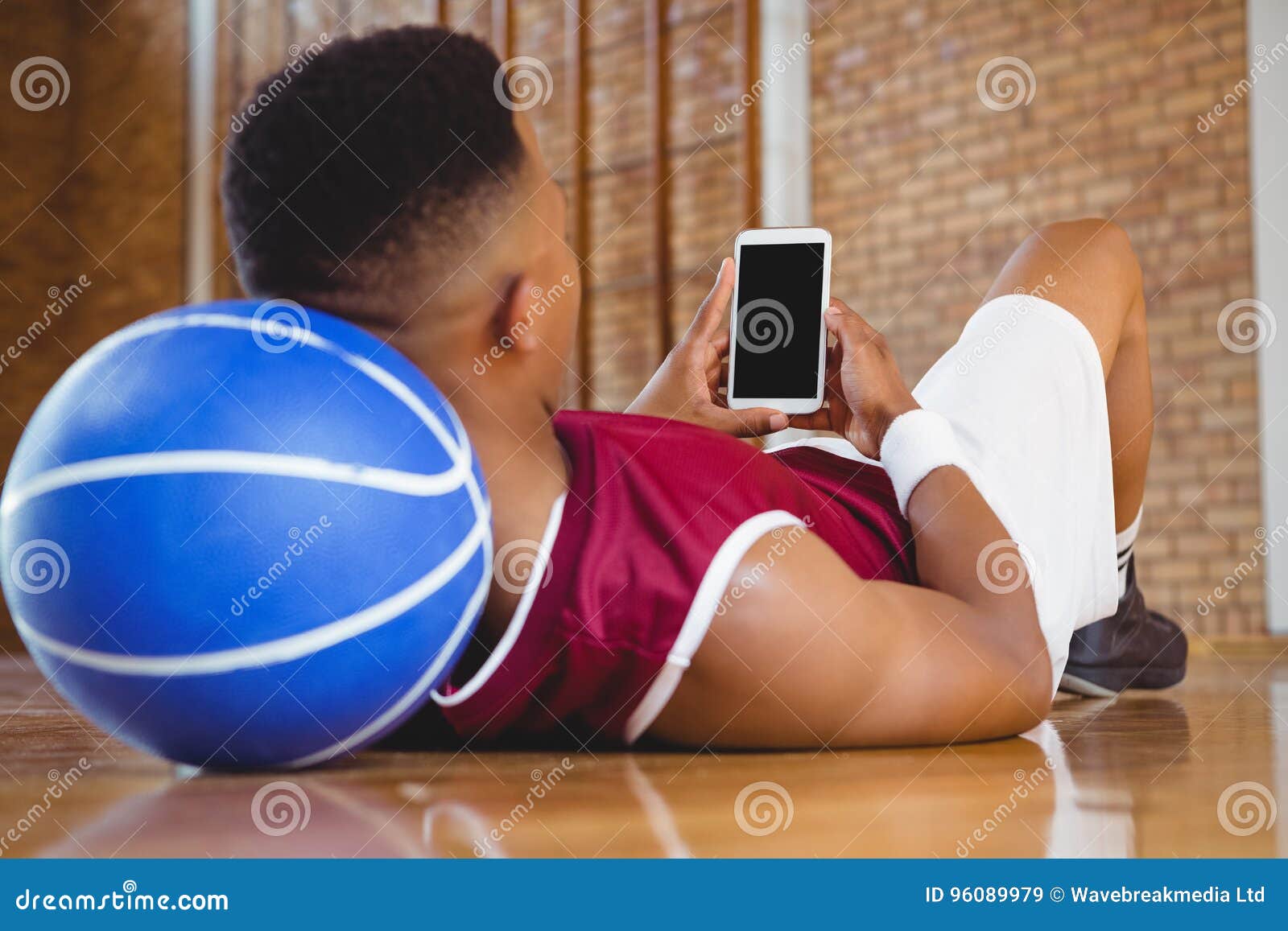 close-up-male-basketball-player-using-mobile-phone-reclining-floor-court-96089979.jpg